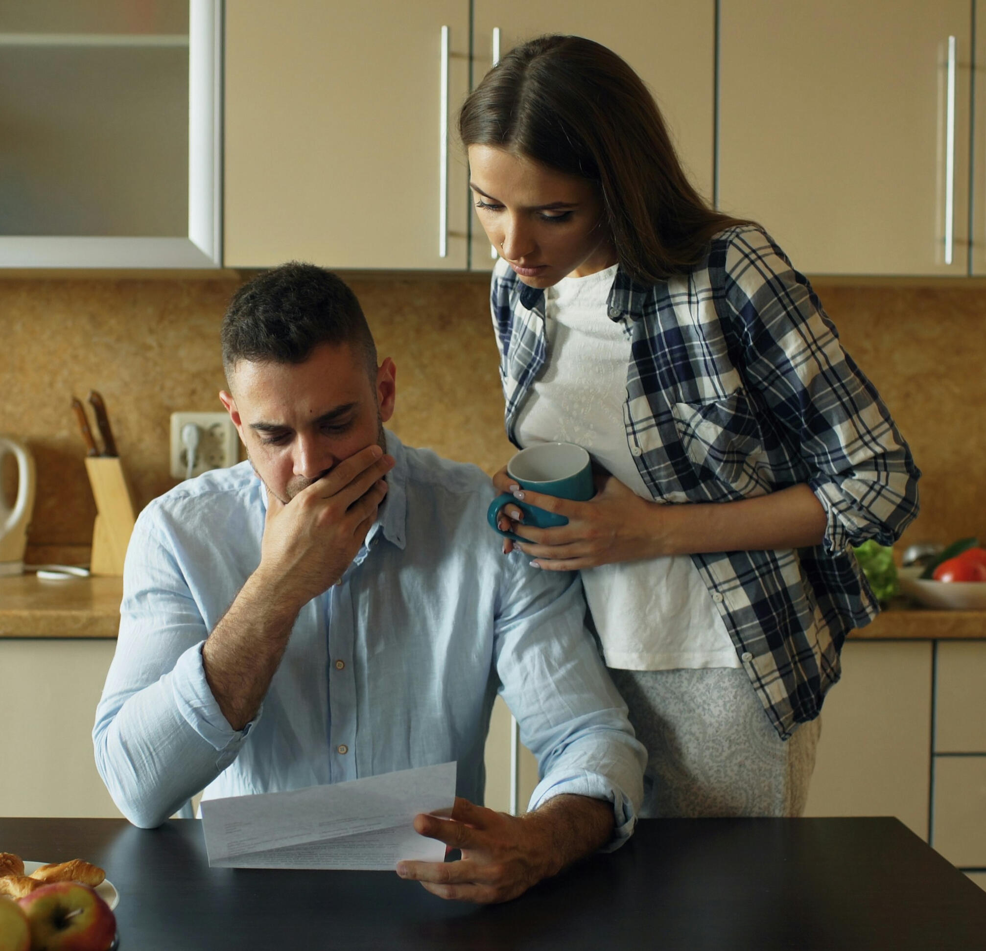 A couple at their kitchen table reviewing paperwork together, both looking worried